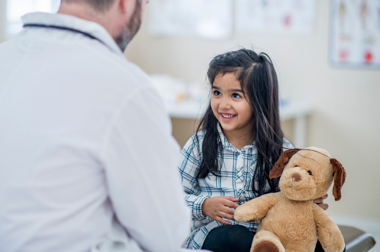 Child Smiling with bear looking up to doctor